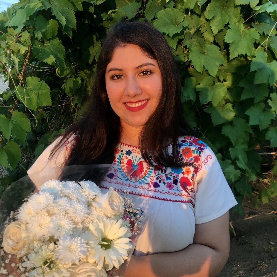 Woman in a multi-colored shirt holding a bouquet of white flowers.