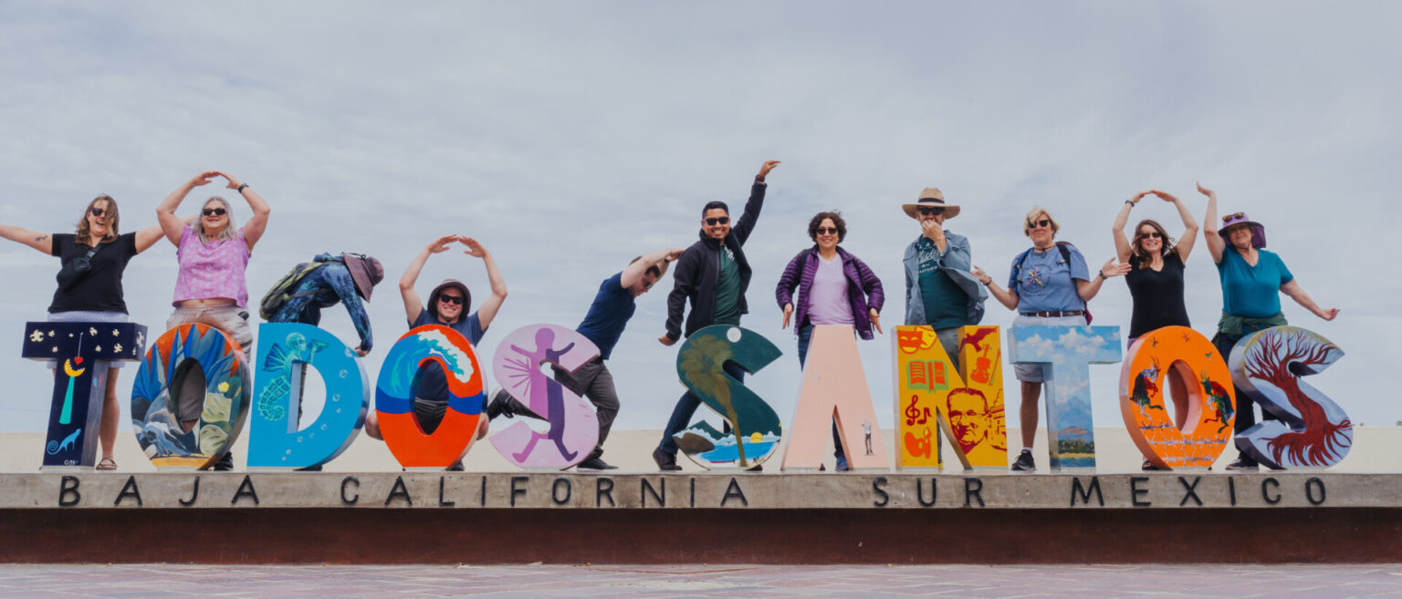 Group photo near a sign that spells out Todos Santos in large block letters.